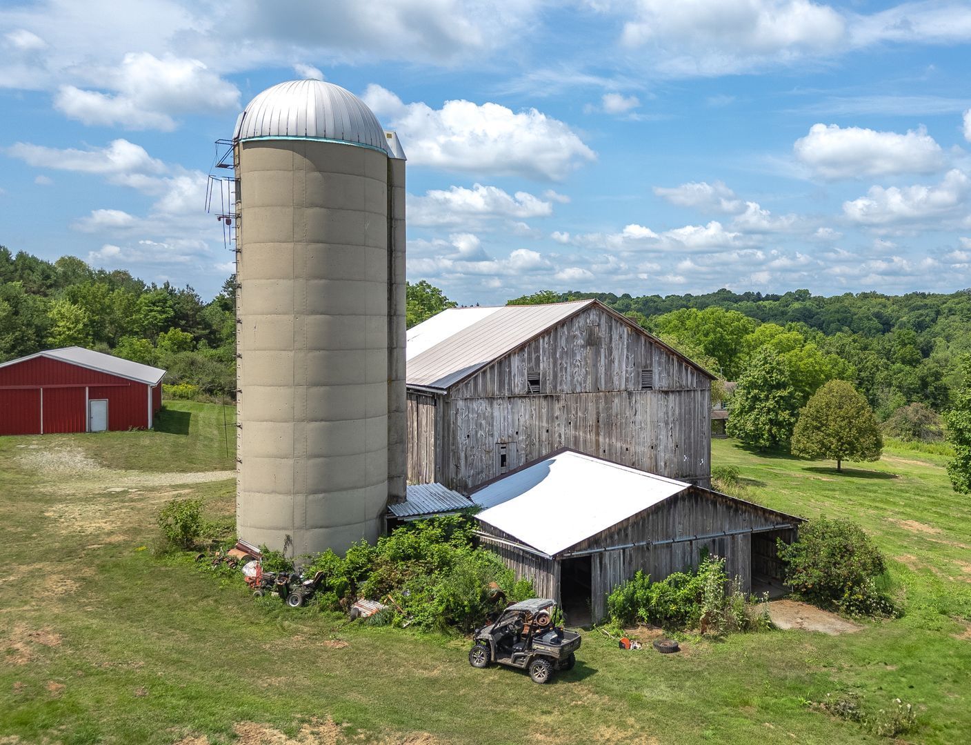 An aerial view of a barn with a silo and a atv parked in front of it.