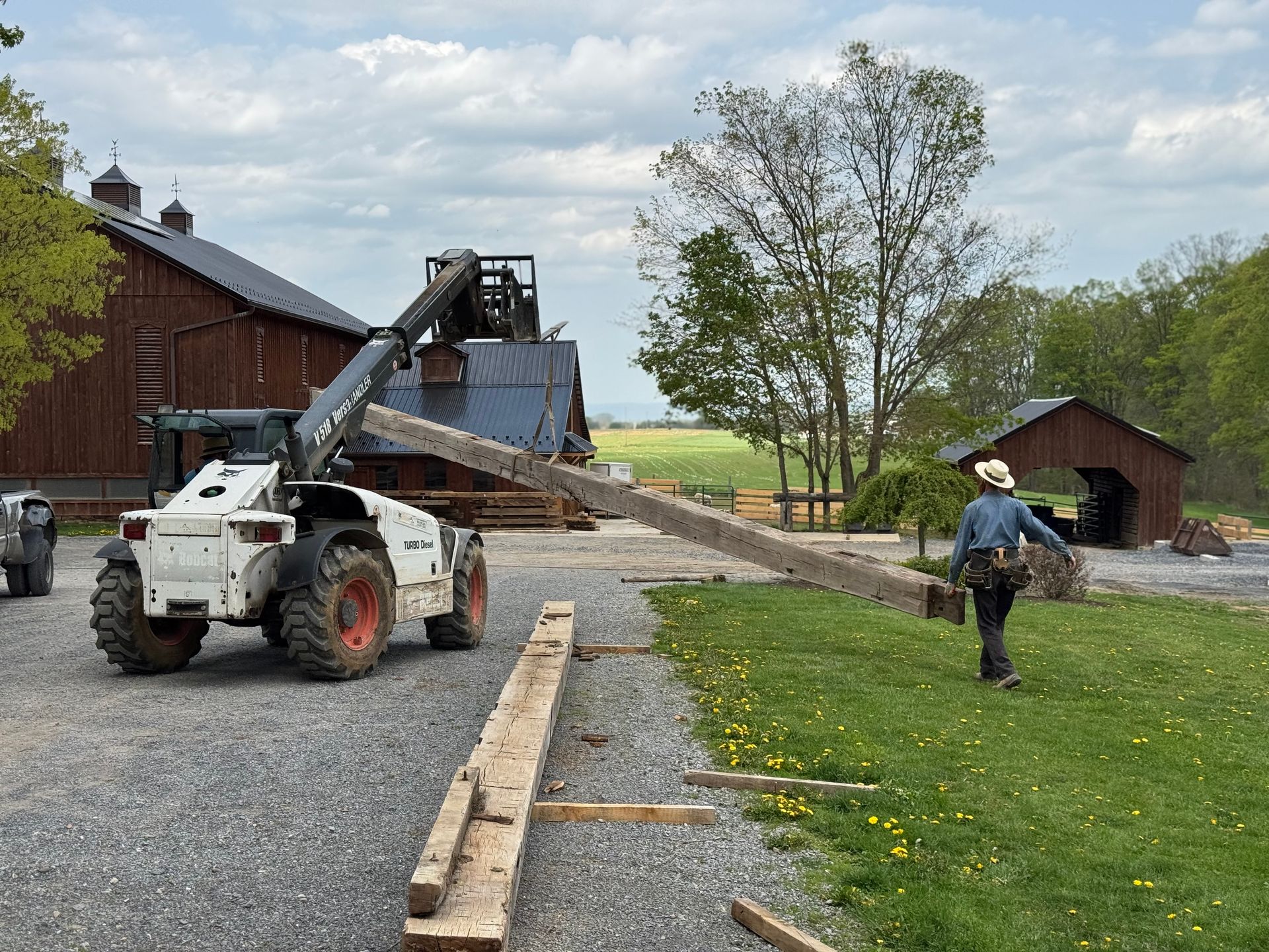 A Bobcat telehandler and a worker move a large wooden beam during a barn demolition near me.