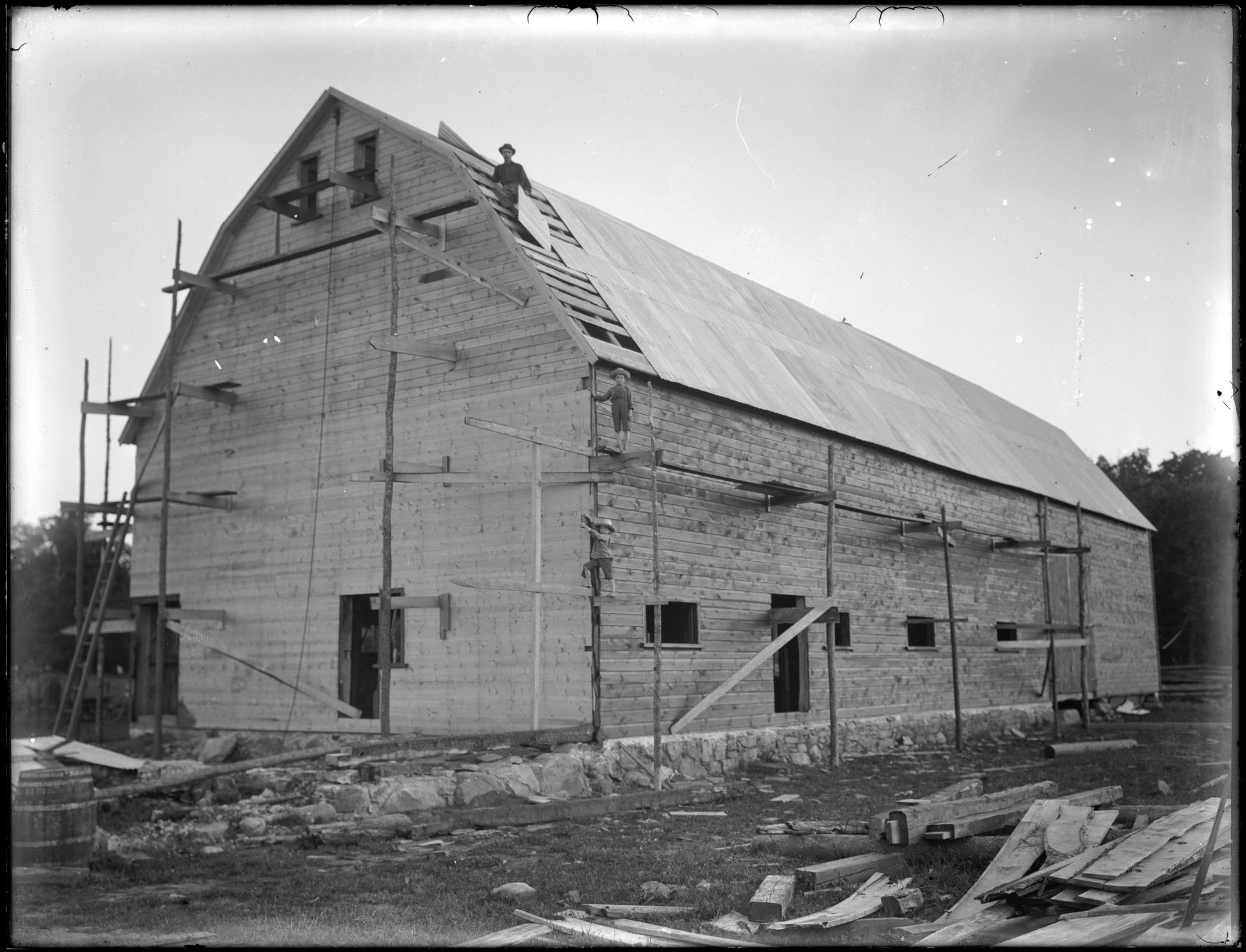 A black and white photo of a barn under construction.