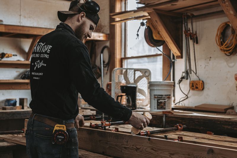 Woodworker applying glue to plank for barn frame restoration.
