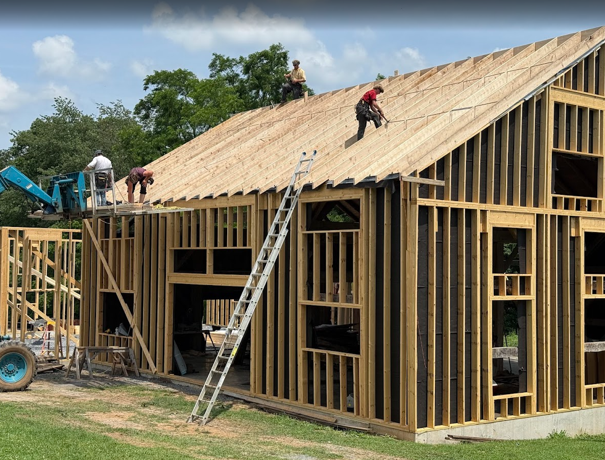 A large house is being built in the middle of a field surrounded by trees.