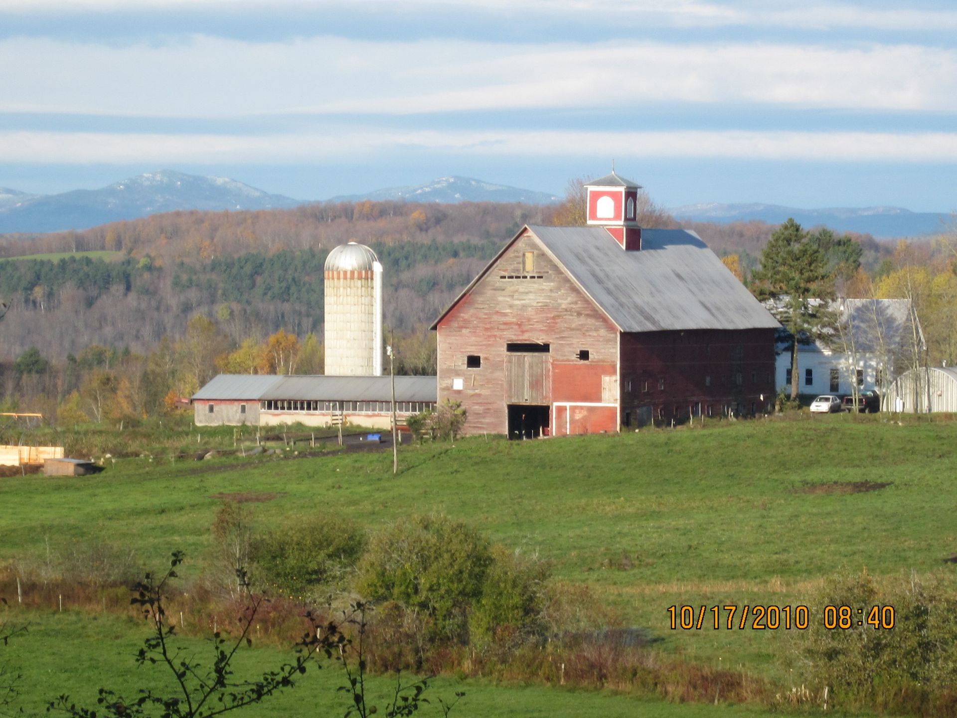 Autumn farm scene with red barn styles, silo, farmhouse, and rolling hills.