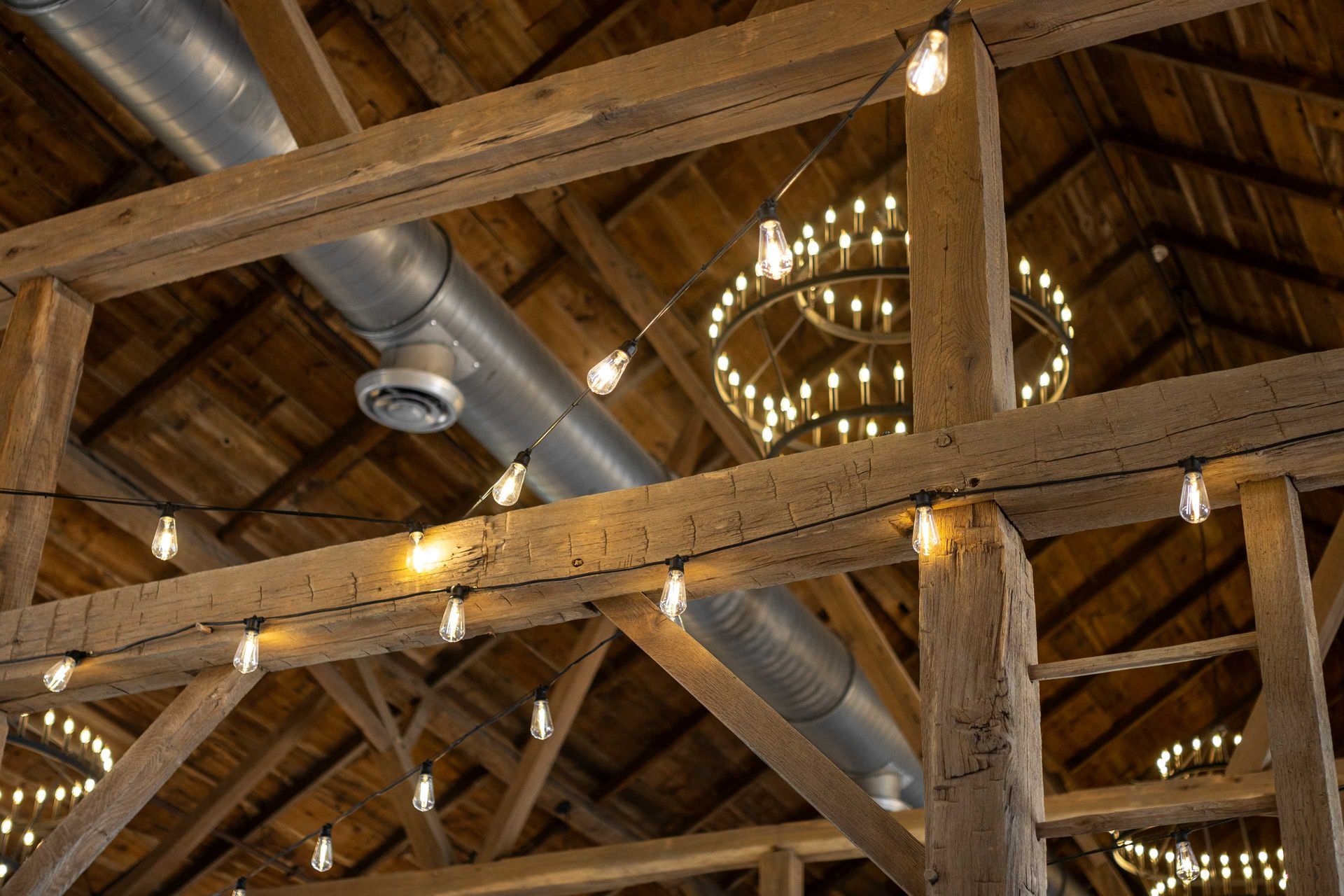 Wooden beams and string lights in a renovated barn highlight architectural restoration.
