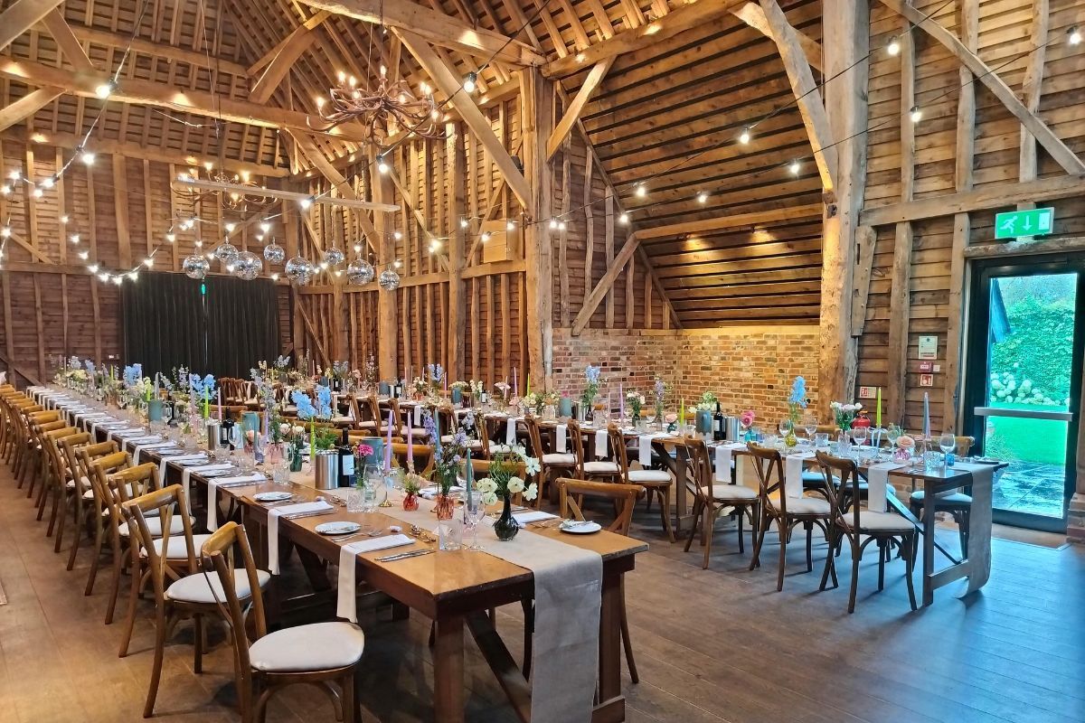 Warmly lit rustic interior with long banquet tables, florals, and disco balls, showcasing an elegant event barn setup.