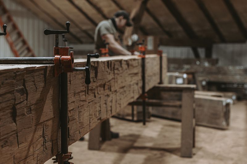 Wooden beam clamped in workshop for barn frame restoration.