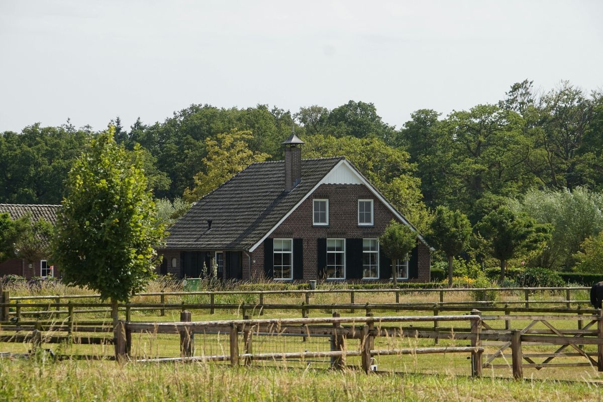 Brick ranch building with dark shutters, gabled roof, wooden fence, and lush greenery.