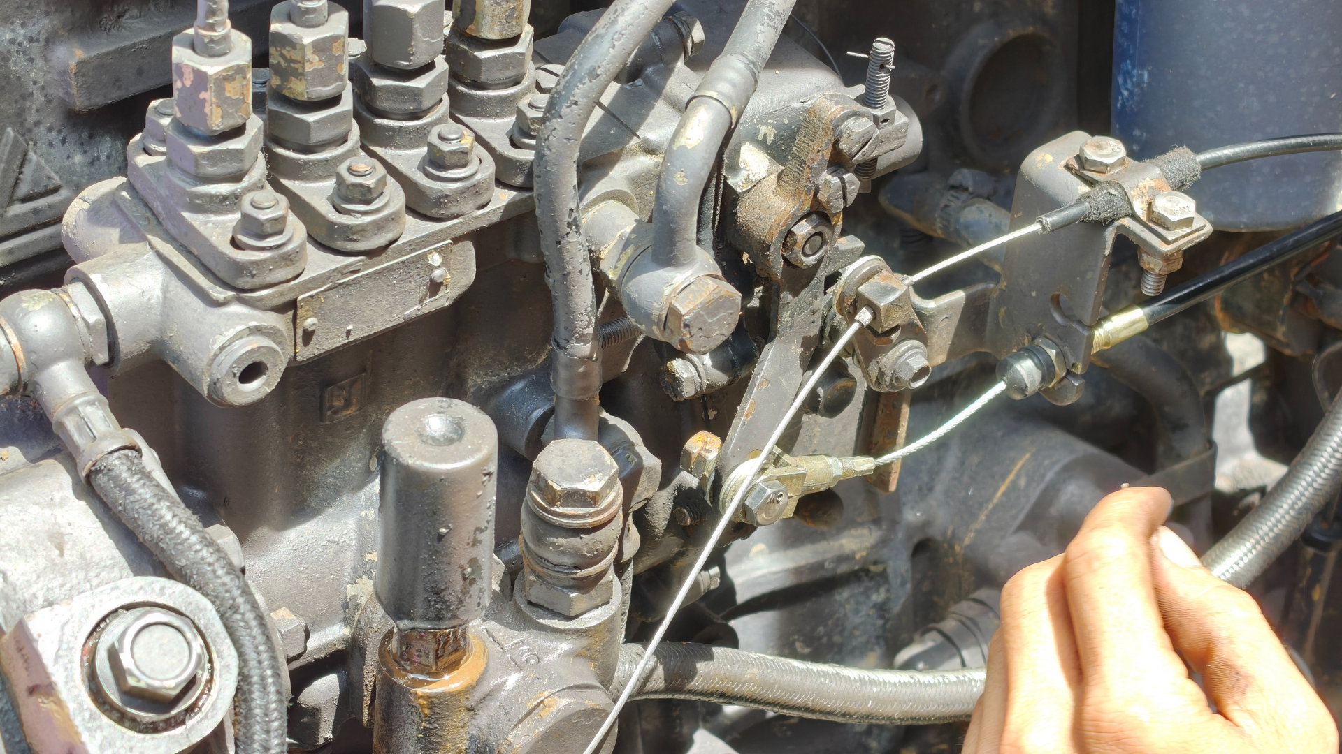 A close-up view of a hand adjusting the throttle cable connected to a mechanical diesel fuel injection pump on an engine.