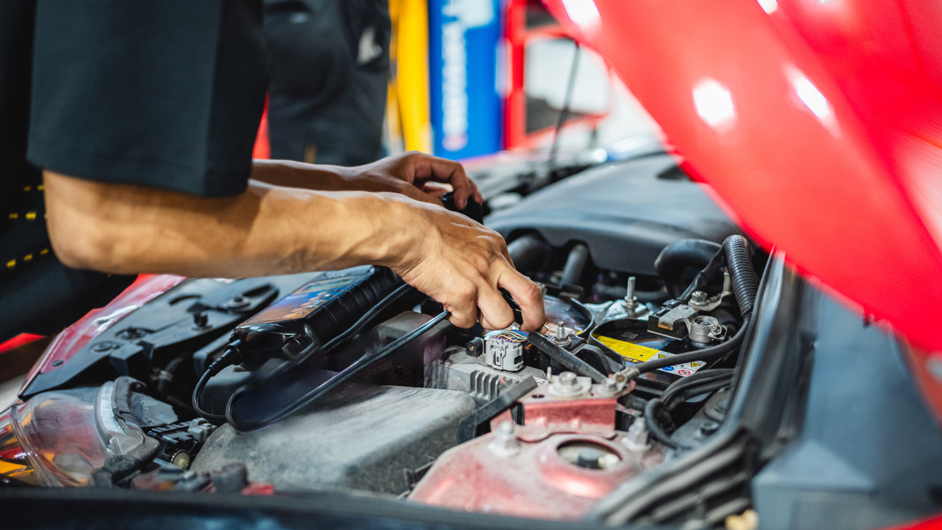 A mechanic working on the engine of a red car in a garage.