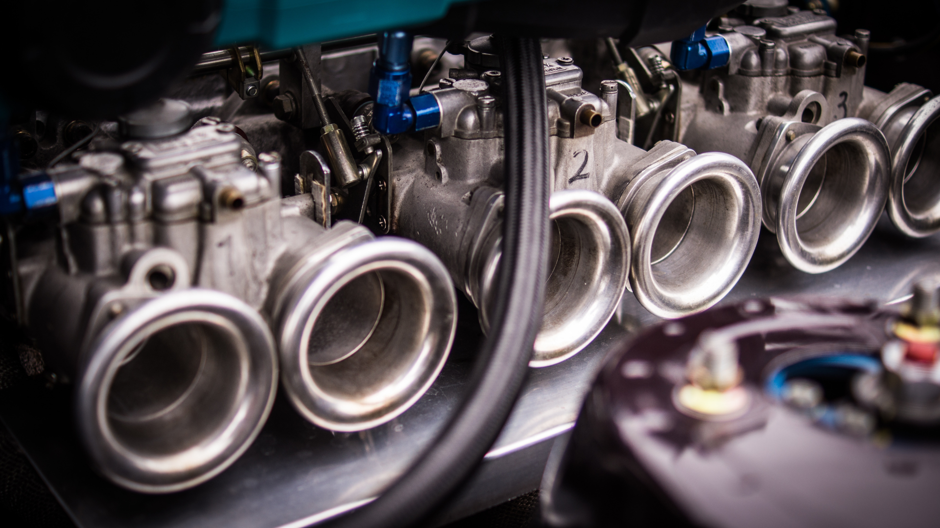 Close-up of a high-performance engine's multiple metallic carburetor air horns mounted in a row.