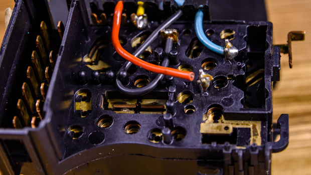 Close-up of a black plastic electrical component with orange, grey, and blue wires soldered to copper contacts.