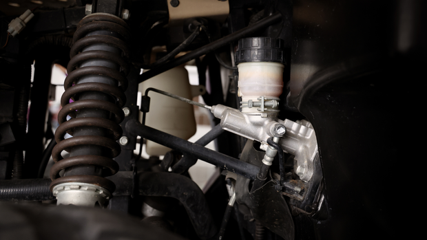 Close-up of a vehicle's brake master cylinder reservoir and suspension coil spring inside the wheel well.