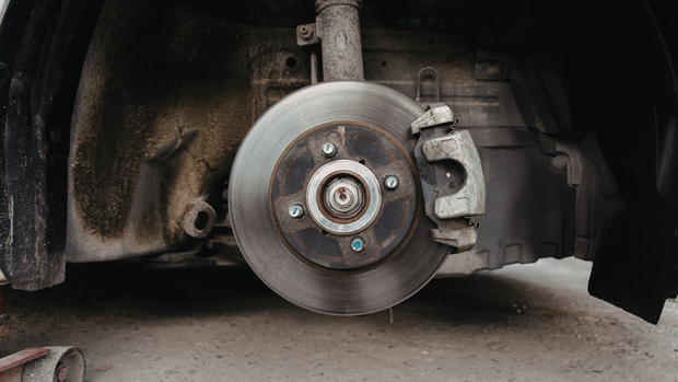A close-up view of a car’s brake disc and caliper assembly with the wheel removed, showing the rotor and wheel hub.