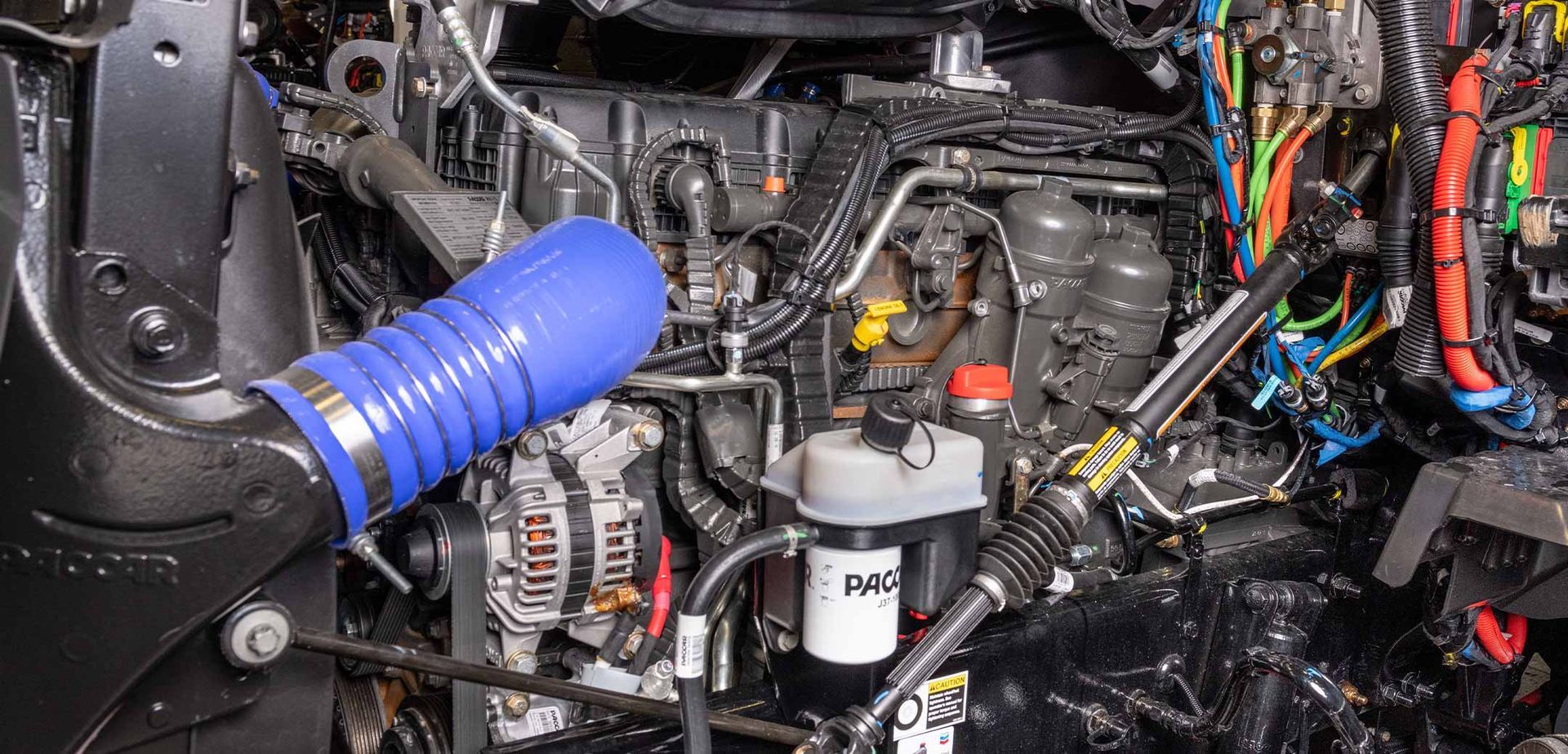 A close-up of a heavy-duty diesel truck engine featuring a prominent blue air intake hose and an Iveco fuel filter.