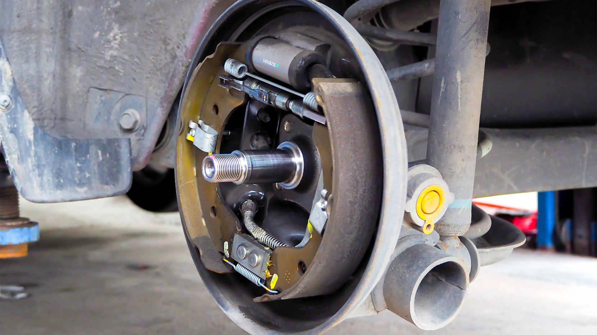 A close-up view of an automobile's rear drum brake assembly, showing the brake shoes, wheel cylinder, and wheel spindle.