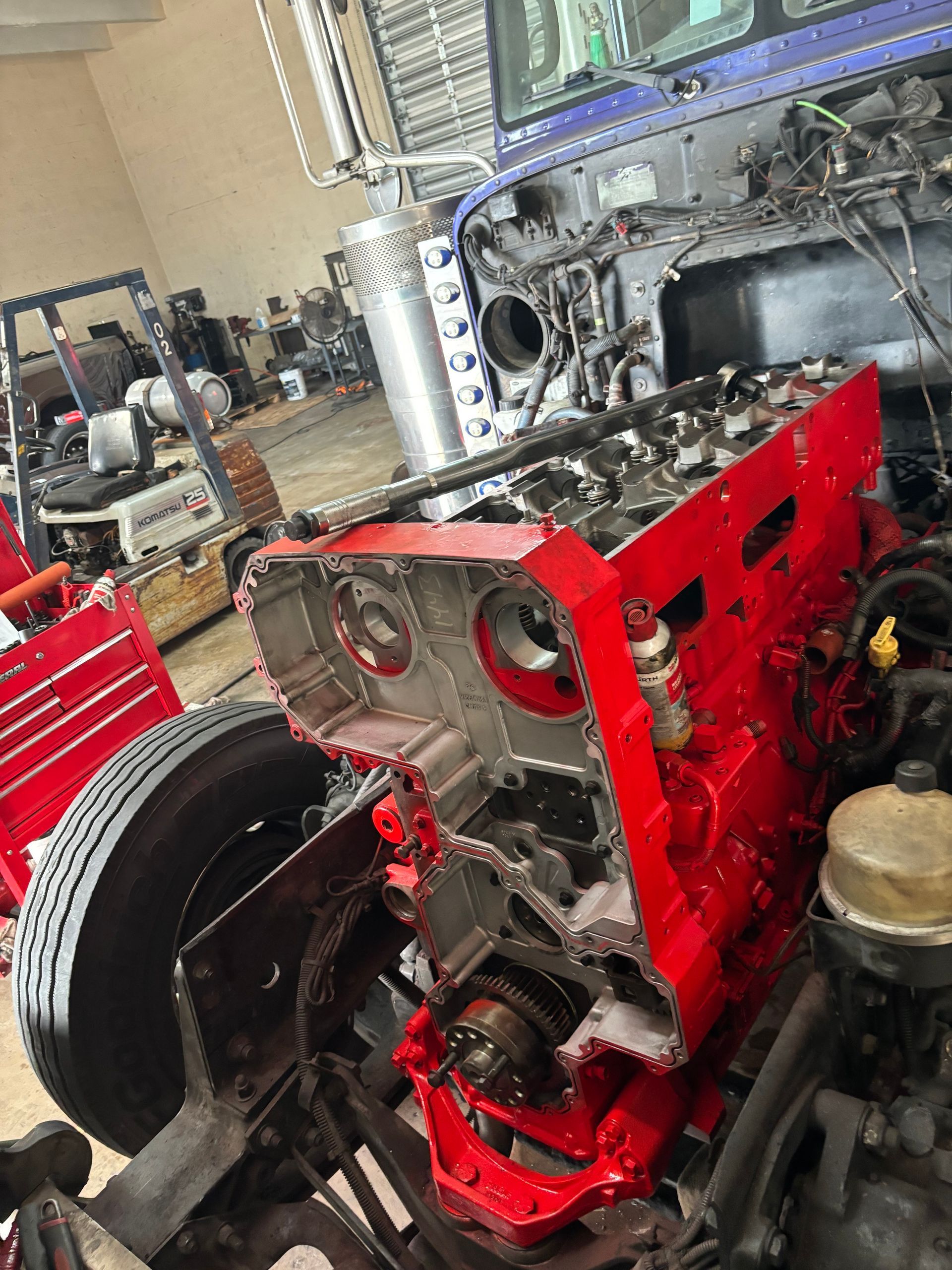 A partially disassembled truck engine painted bright red sits in a vehicle repair shop.