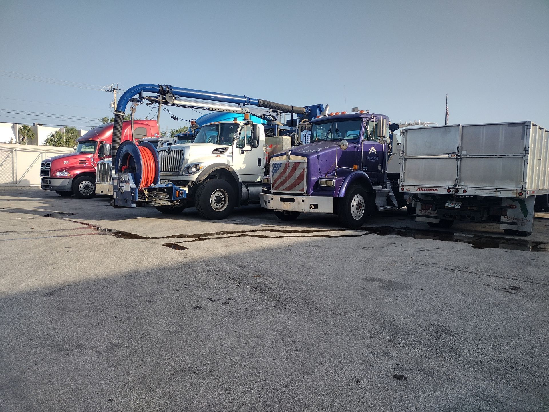 Three large industrial trucks, including a vacuum truck, parked in a row on a gravel lot under a clear sky.