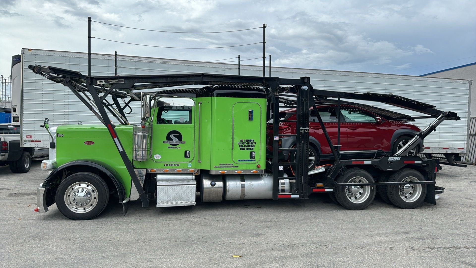 A bright green car carrier semi-truck with a red vehicle loaded on its trailer, parked on a gravel lot.