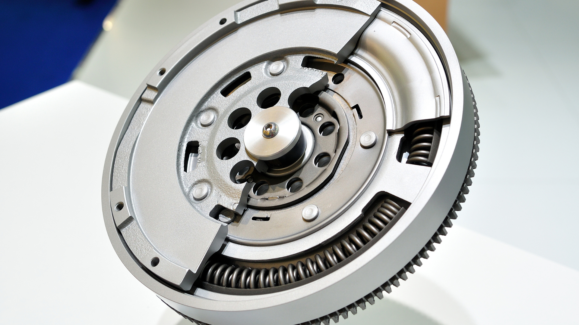 A dual-mass flywheel showing internal springs and mechanical components set against a neutral, light-colored background.