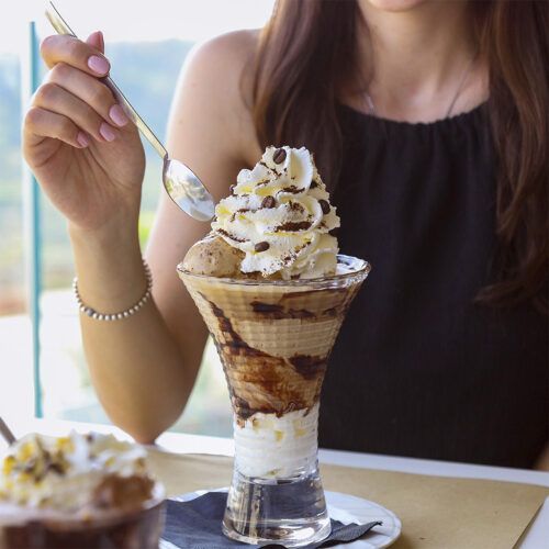 Donna che mangia una coppa gelato con panna montata e scaglie di cioccolato.