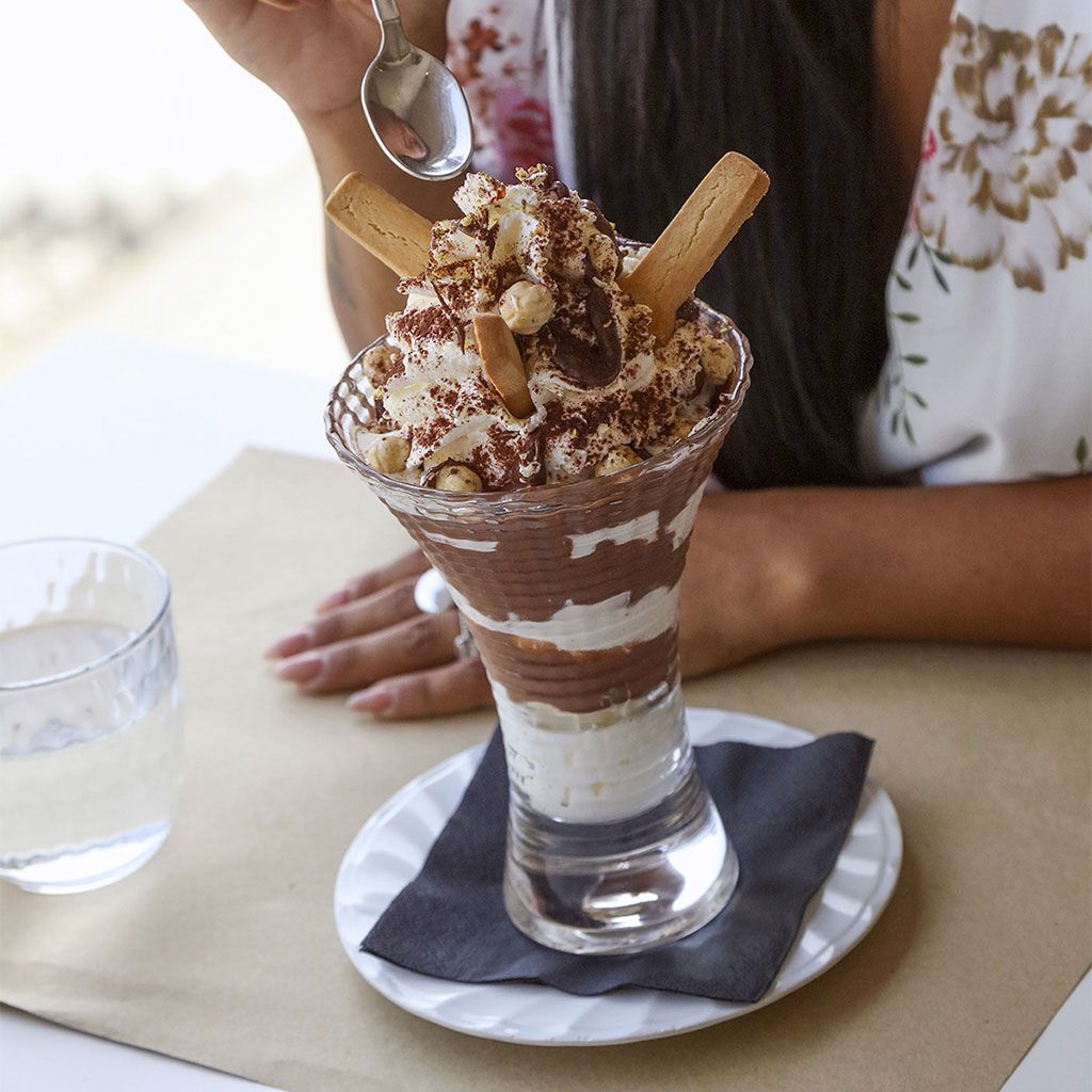 Parfait di dessert in un bicchiere, con panna montata, cacao e biscotti.