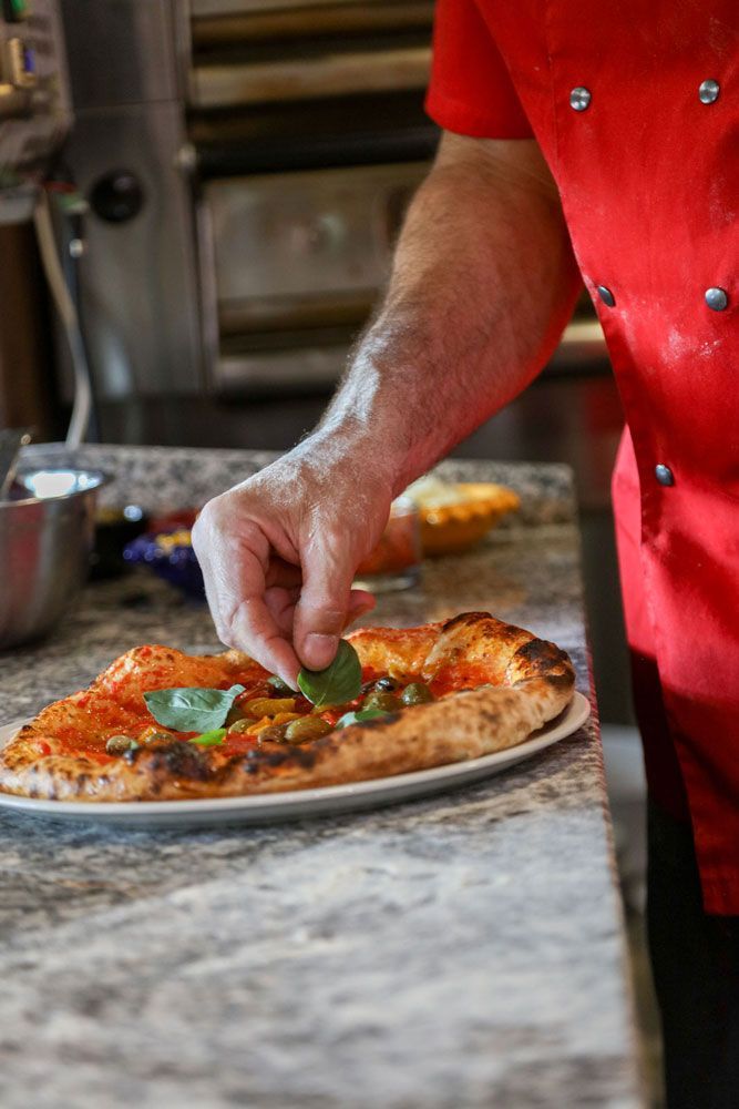 Uno chef guarnisce una pizza con foglie di basilico in cucina.