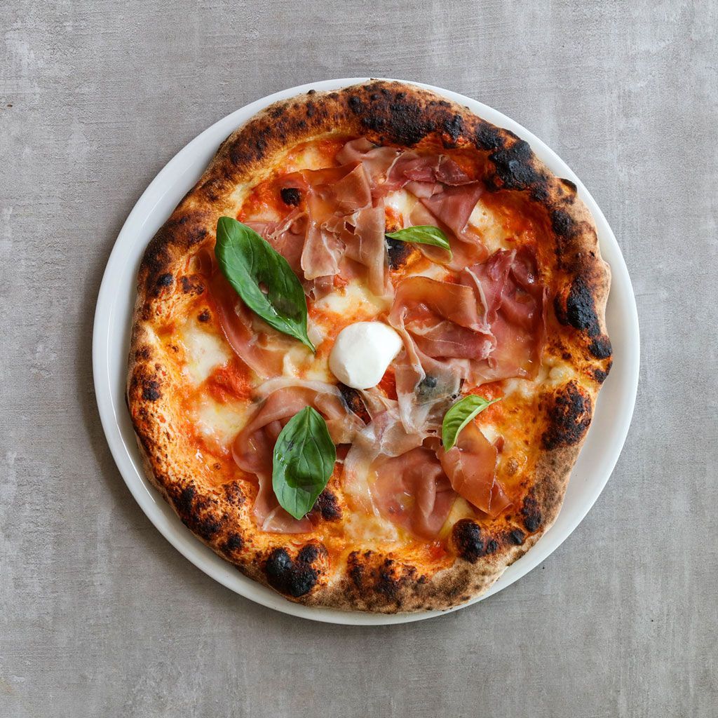 Pizza con prosciutto, basilico e mozzarella su un piatto bianco.