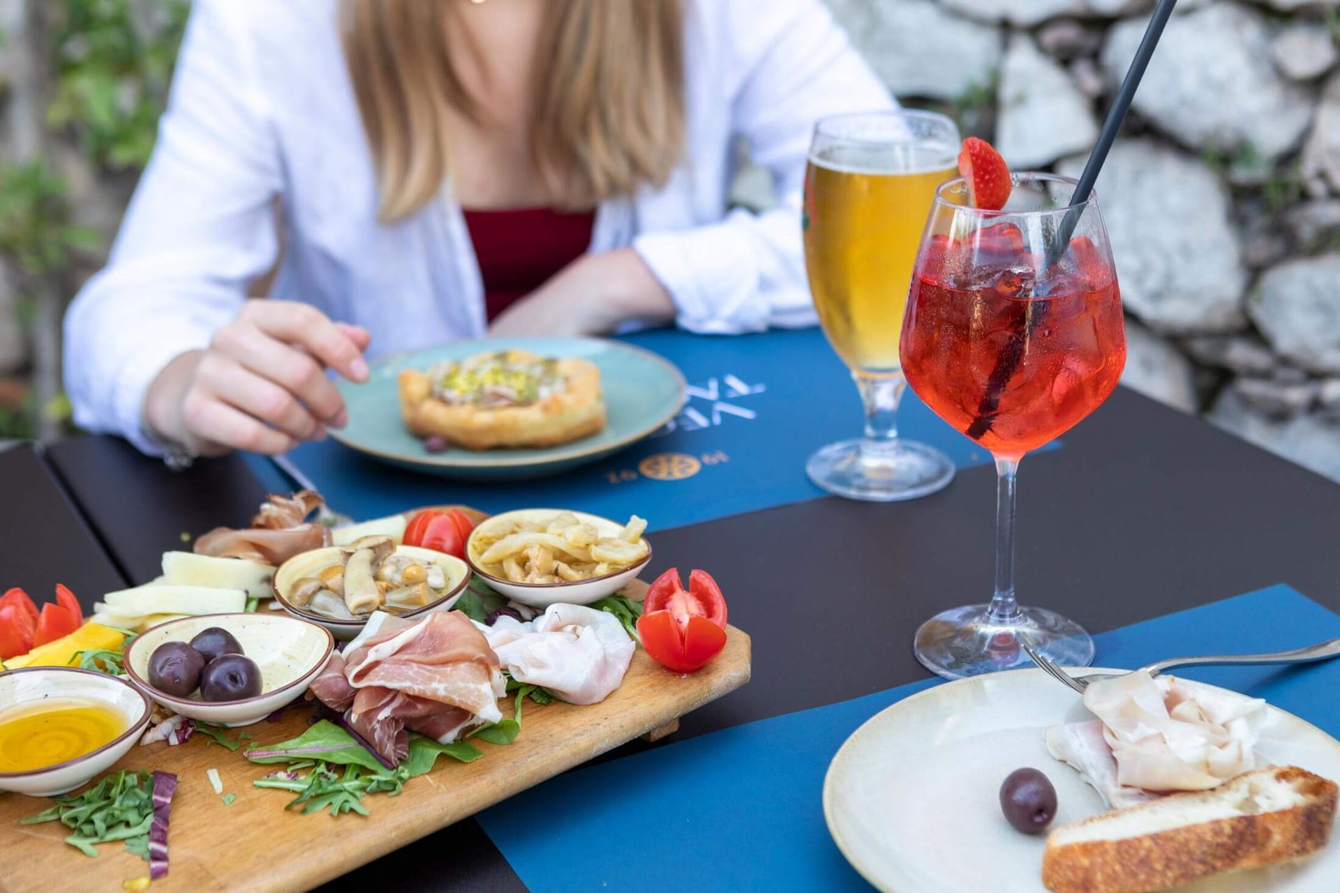 Donna seduta a un tavolo con antipasti e bevande in un ristorante all'aperto.