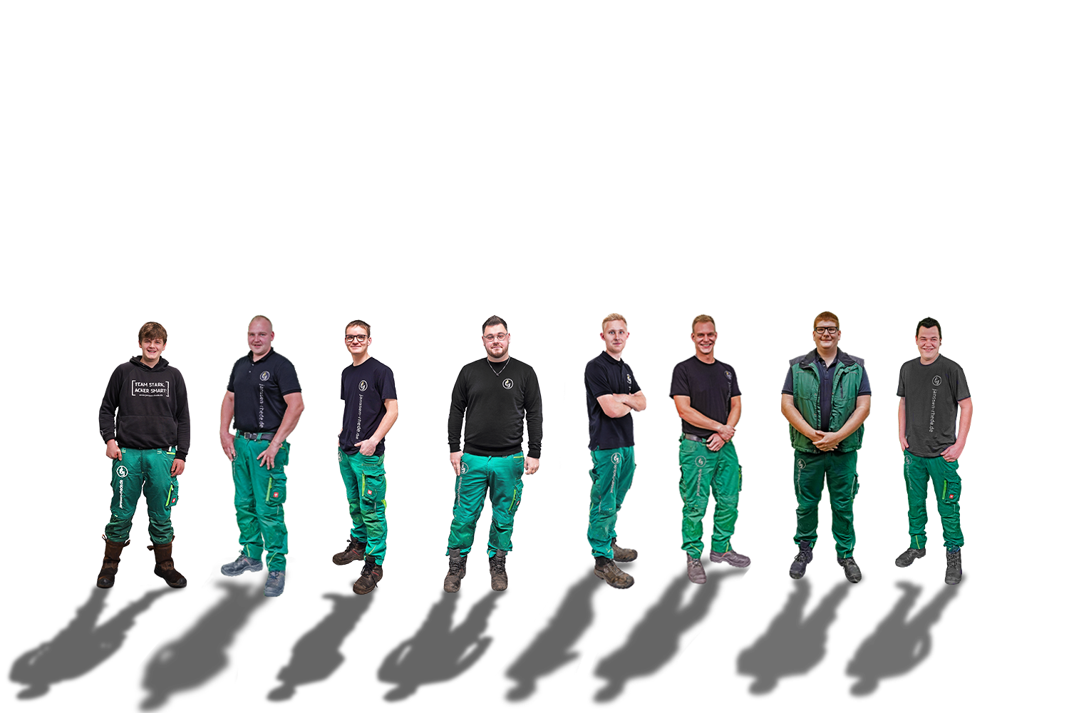 Acht Personen stehen in einer Reihe vor einem weißen Hintergrund; alle tragen grüne Arbeitshosen und dunkle Hemden oder Jacken.