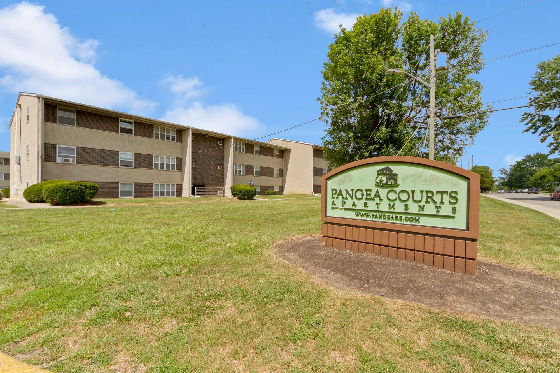 Pandrea Courts Apartments sign in front of a multi-story apartment building with a green lawn on a sunny day.
