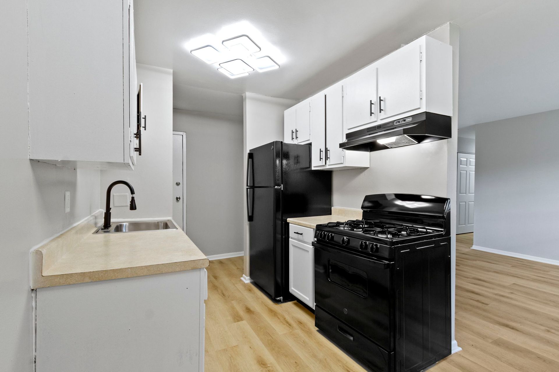 Small kitchen with black appliances, white cabinets, and beige countertops, and wood-look flooring.