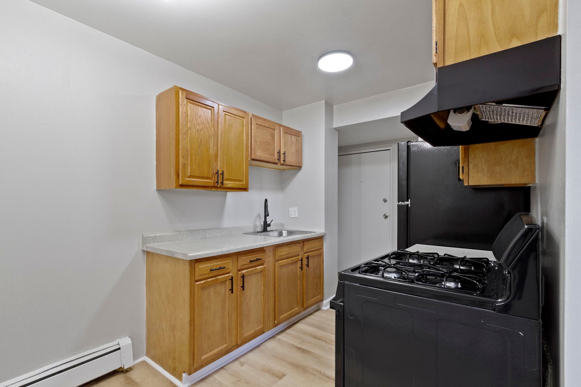 Small kitchen with light wood cabinets, black appliances, and gray walls.