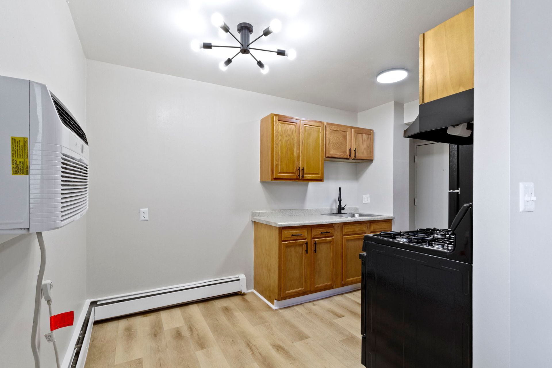 A small kitchen with wooden cabinets, a black stove, and a wall-mounted AC unit.