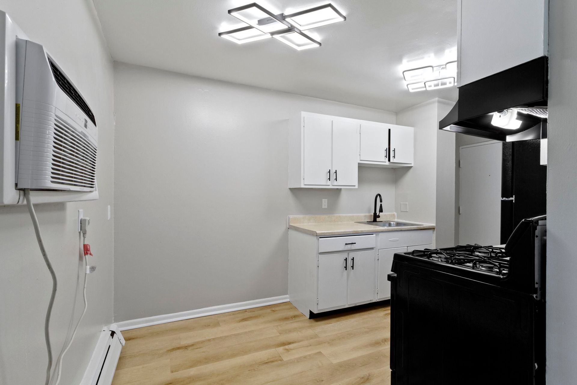 Kitchen with white cabinets, black stove, and a mounted air conditioner.