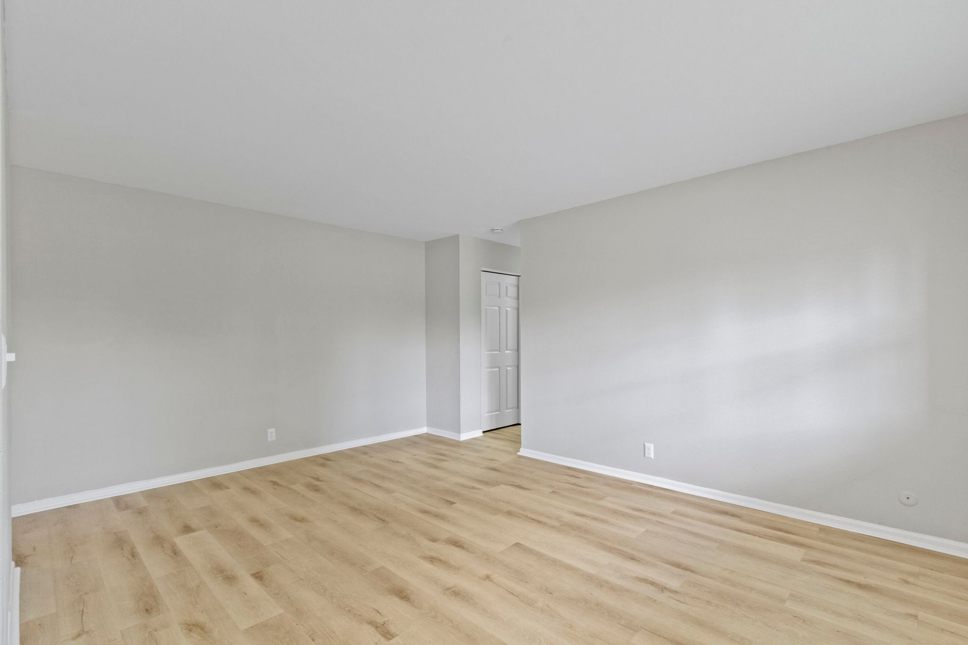 Empty room with wood-look flooring, light gray walls, and a doorway.