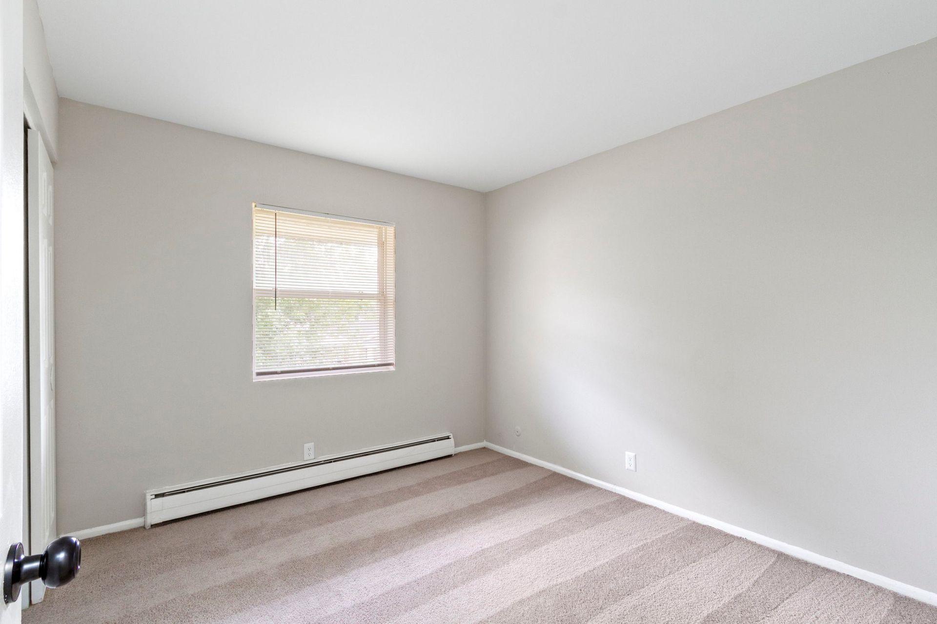 Empty room with beige walls, carpet, and blinds covering a window.