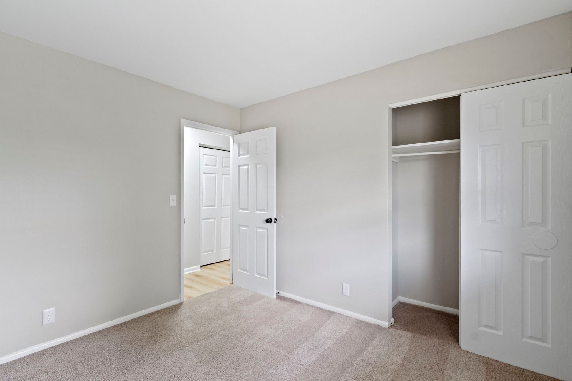 Empty bedroom with beige carpet, gray walls, white doors, and a closet.