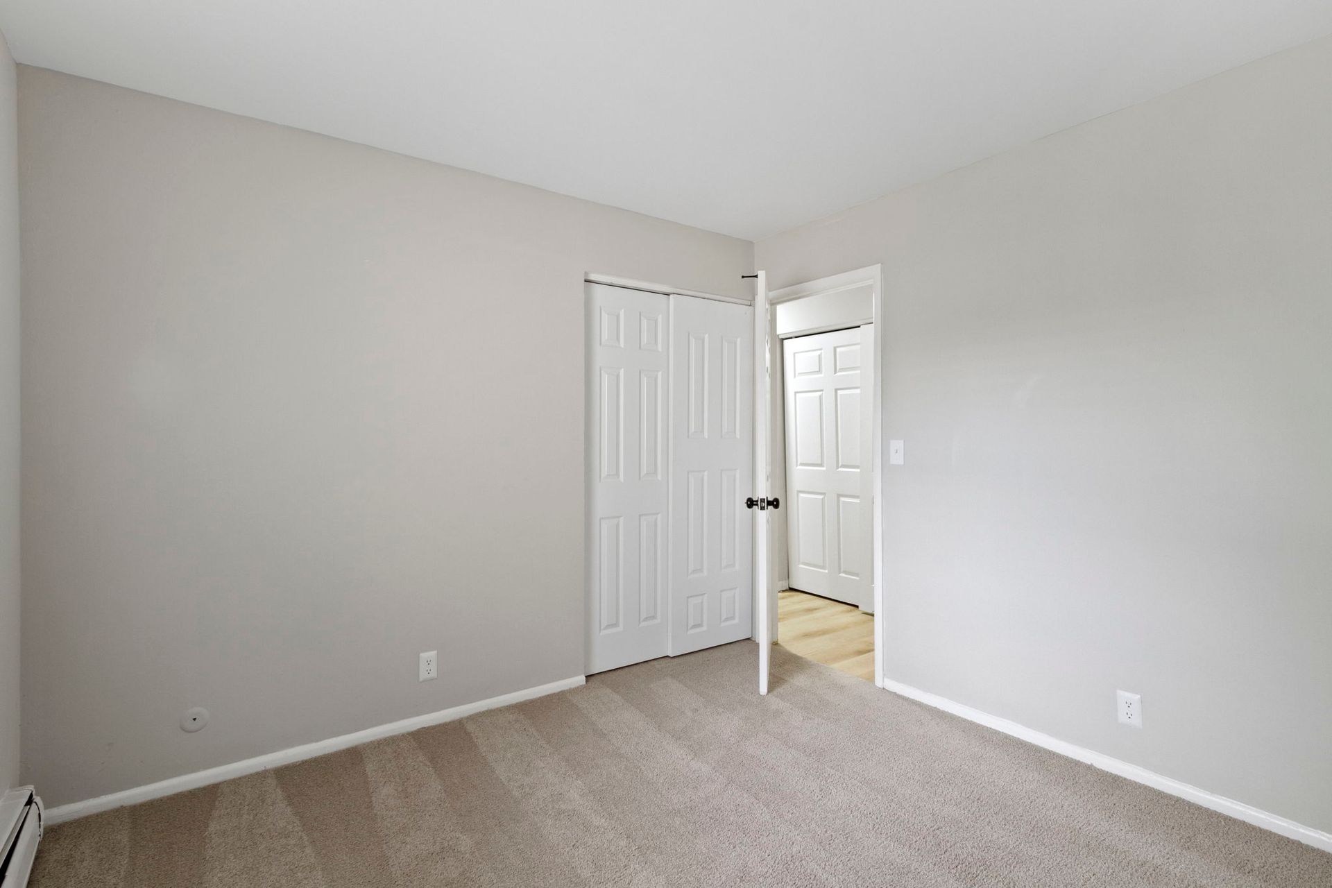 Empty bedroom with beige carpet, light gray walls, and white closet and doors.