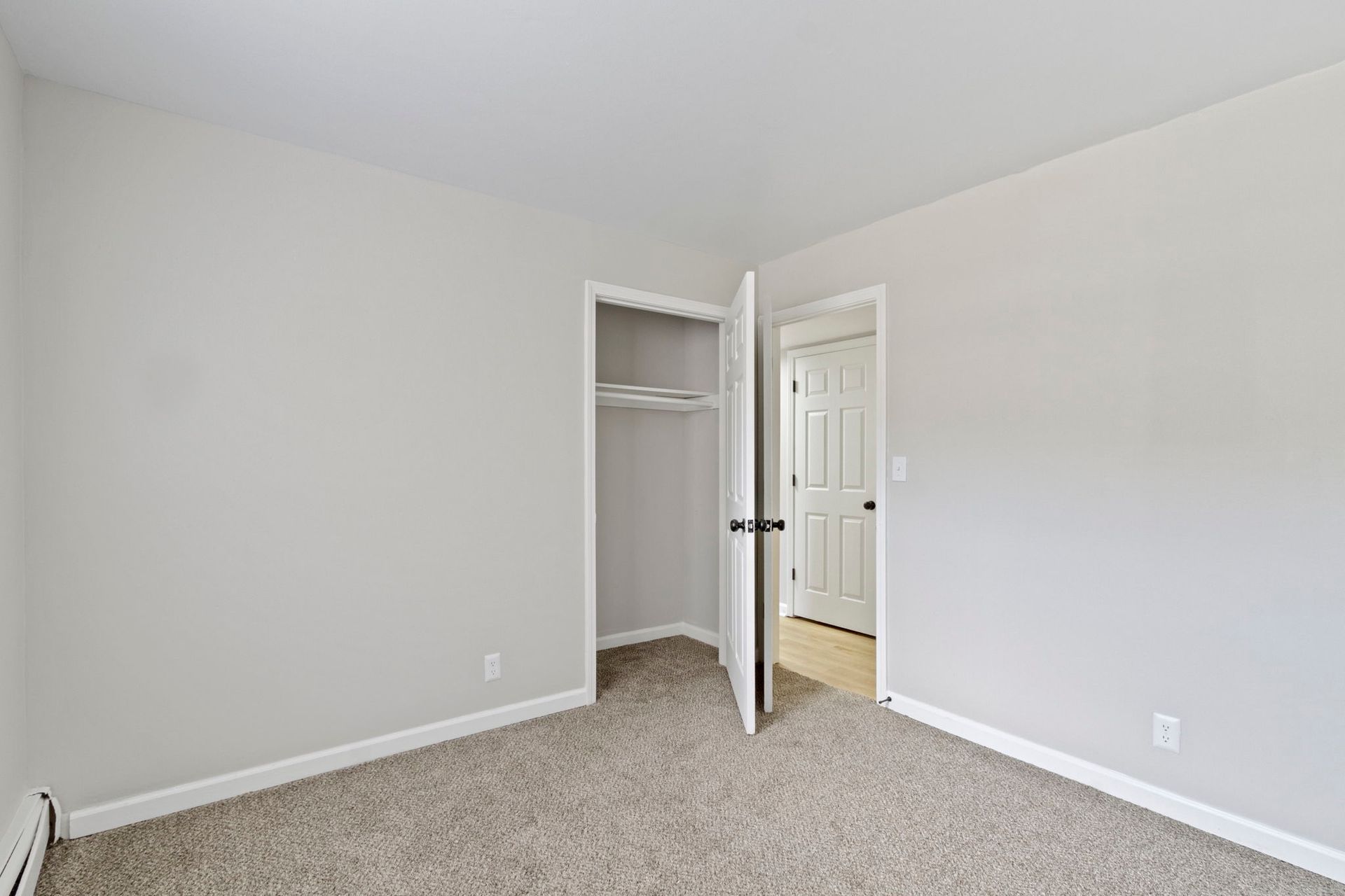 Empty bedroom with light grey walls, carpet, open closet, and a doorway.
