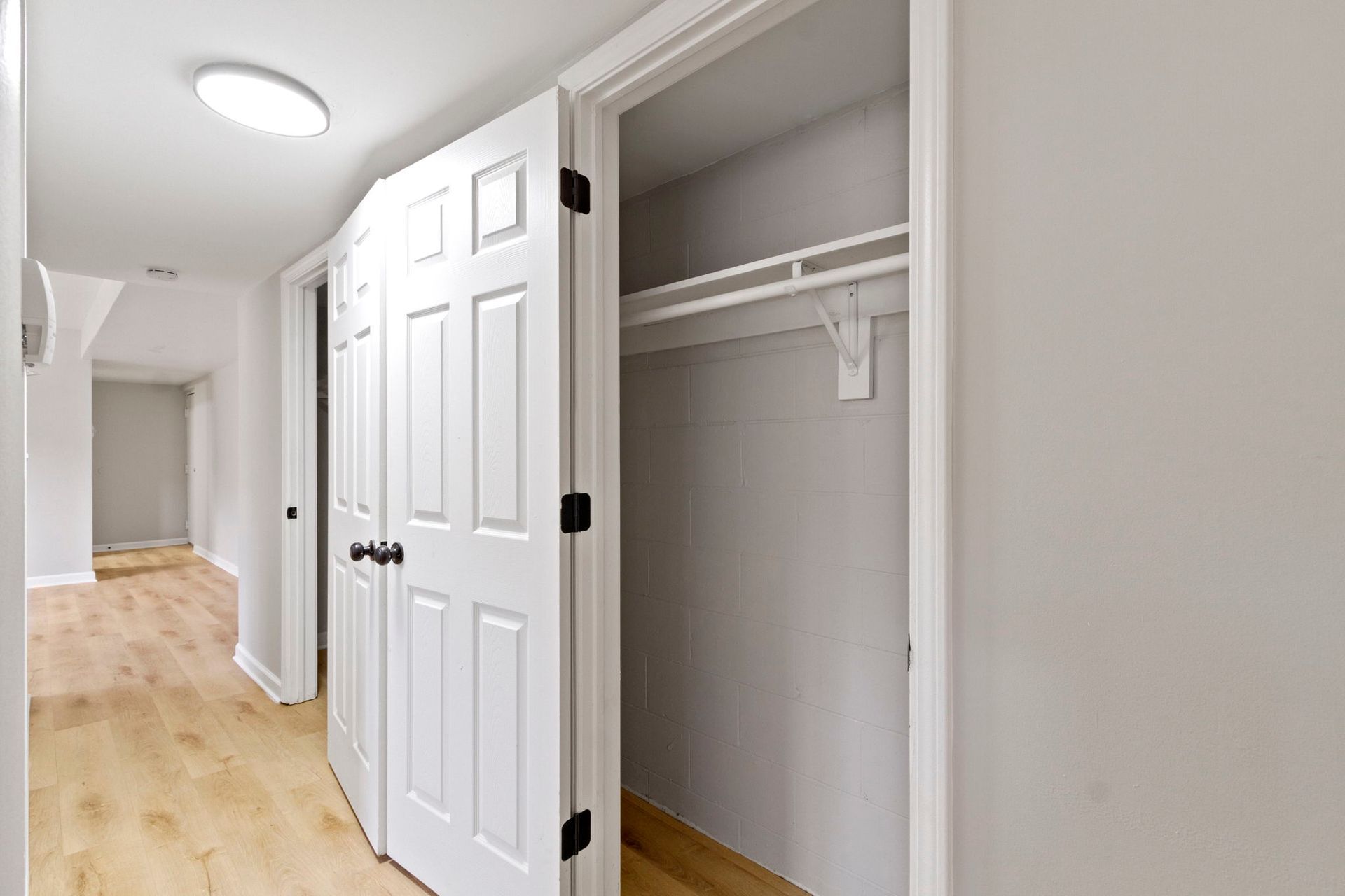 A closet with open white doors in a hallway with light wood floors.