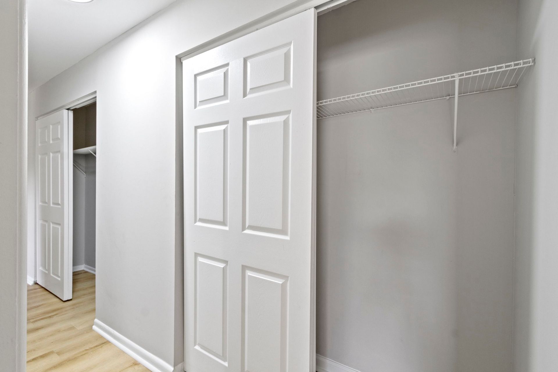 Closet with a sliding door, clothes rack, and door open on the left; white and light gray interior.
