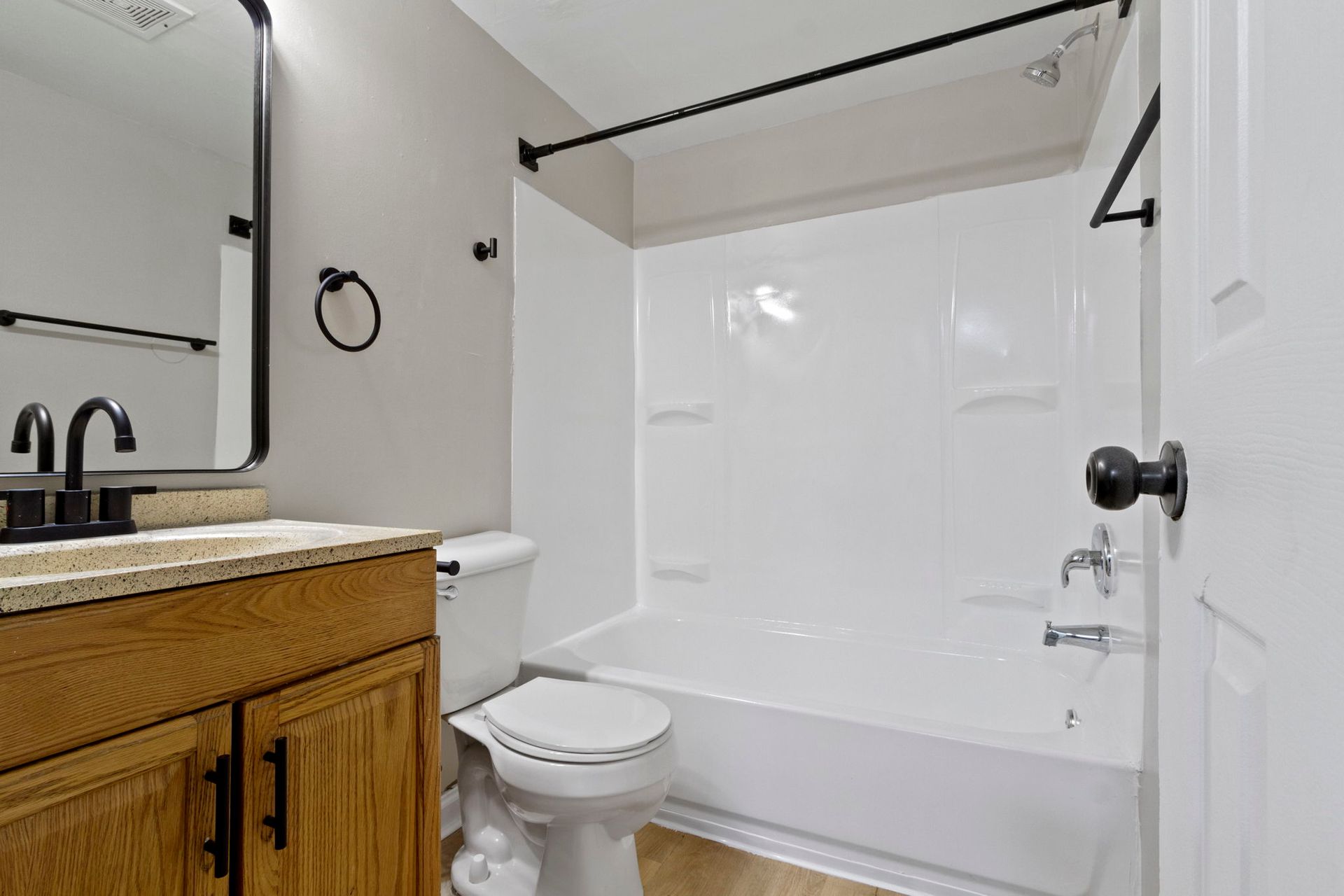 Bathroom with a white shower/tub, toilet, wooden vanity, and black fixtures.