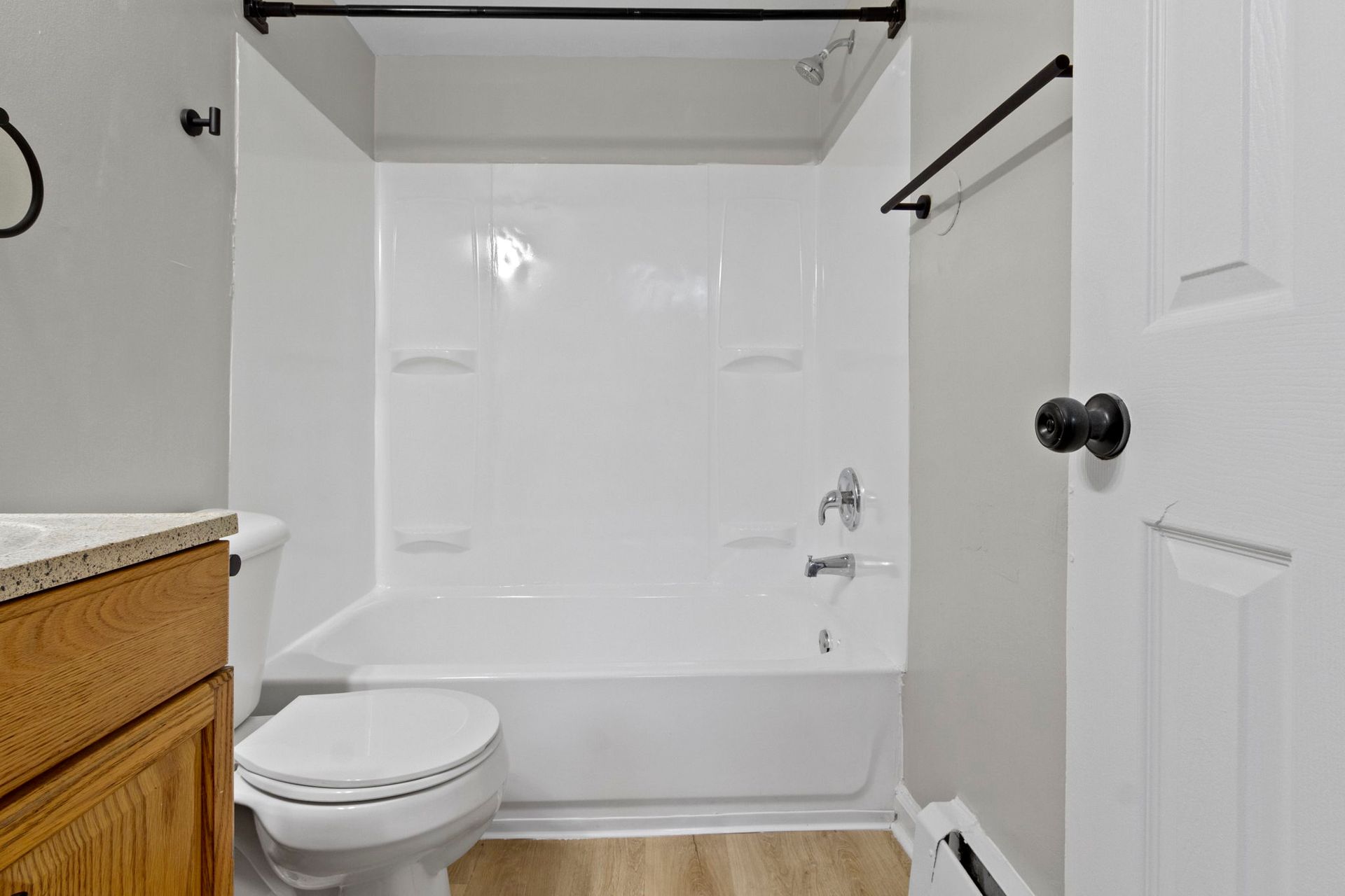 Small bathroom with white bathtub, toilet, and walls, wooden vanity.