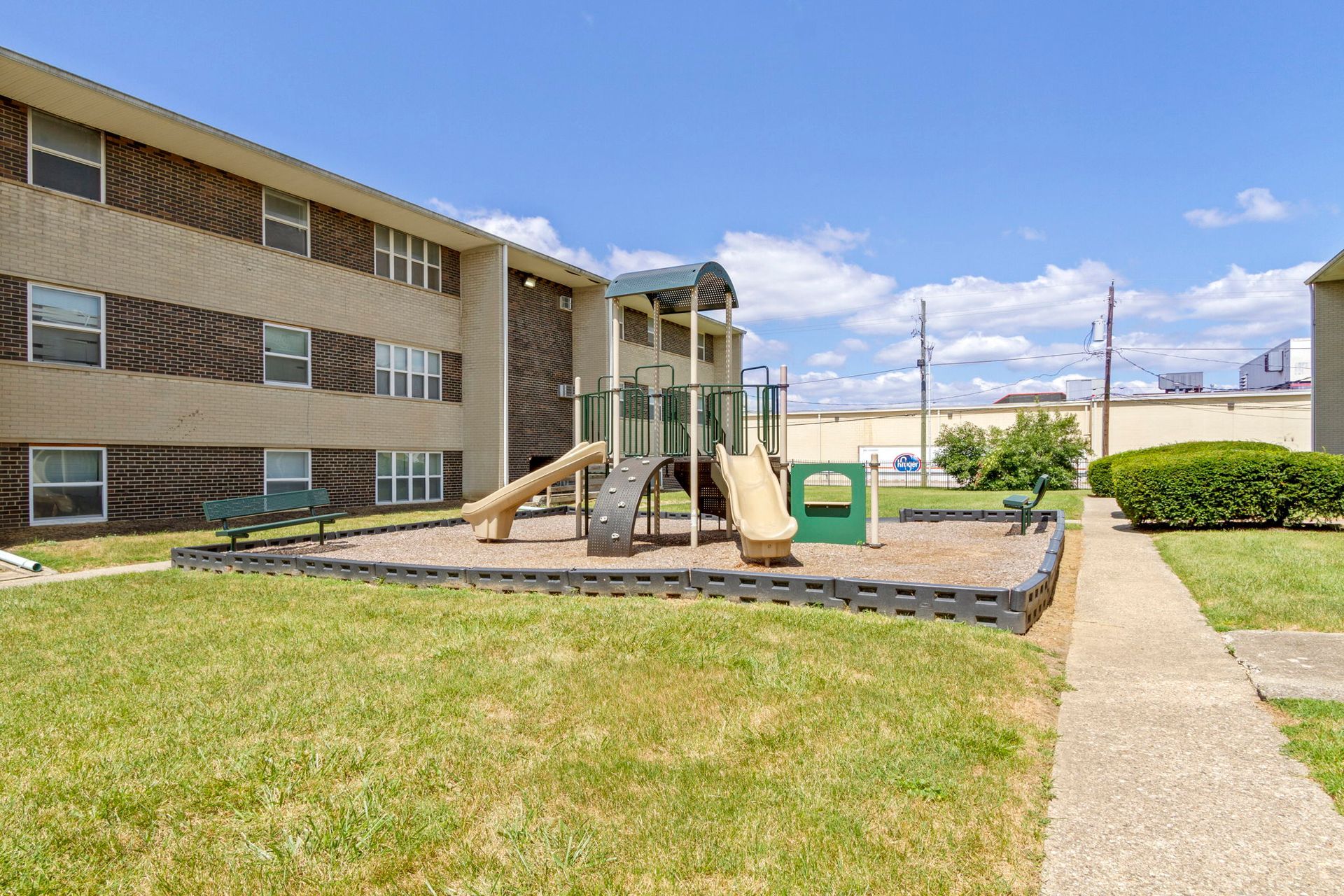 Apartment building with a playground on a grassy lawn under a blue sky.