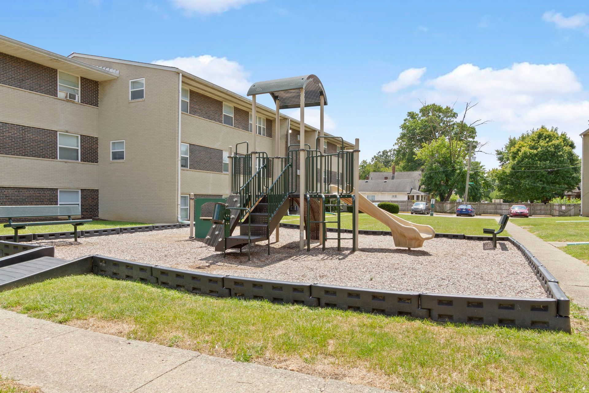 Playground next to apartment building; slide, stairs, ground cover, green grass.