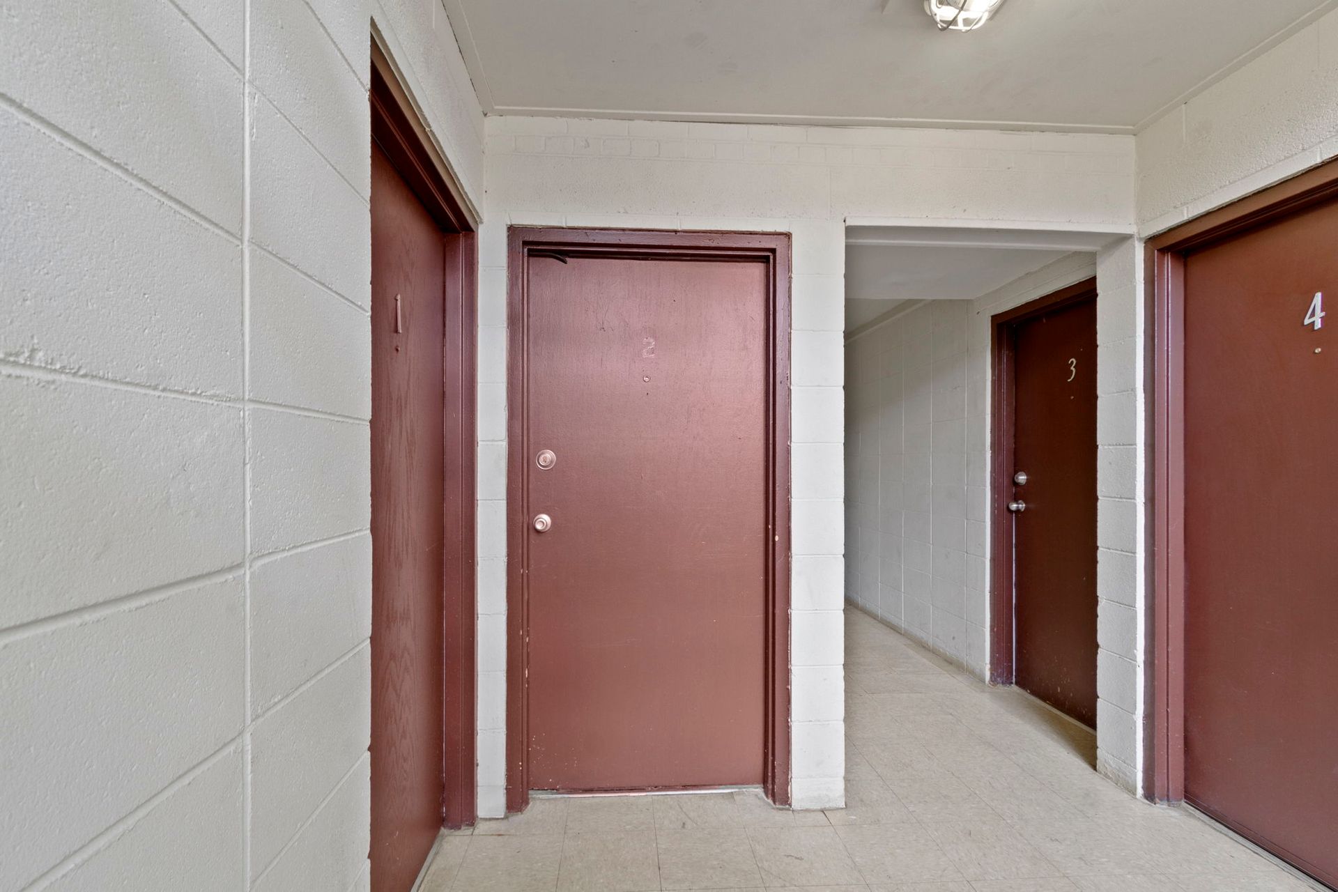 Hallway with four brown doors, white block walls, and a light fixture.
