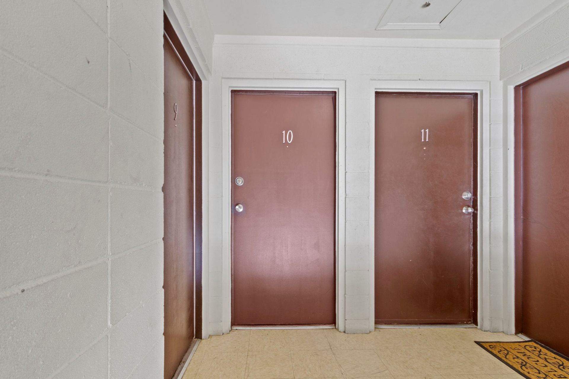 Hallway with three closed brown doors, numbered 9, 10, and 11, on a cream-colored floor.