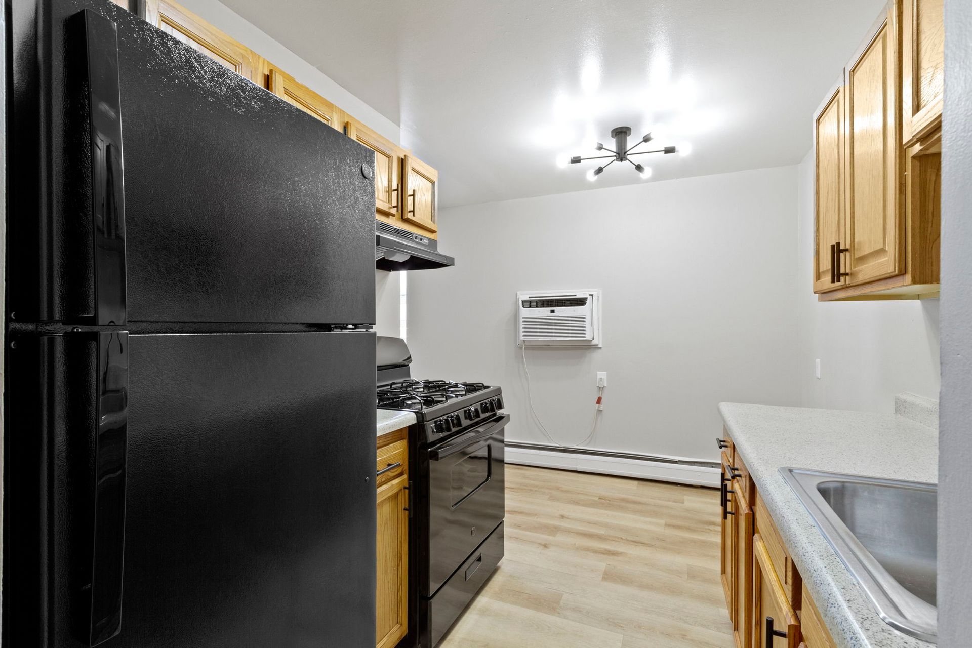 Black appliances in a small kitchen with wood cabinets and light floors.