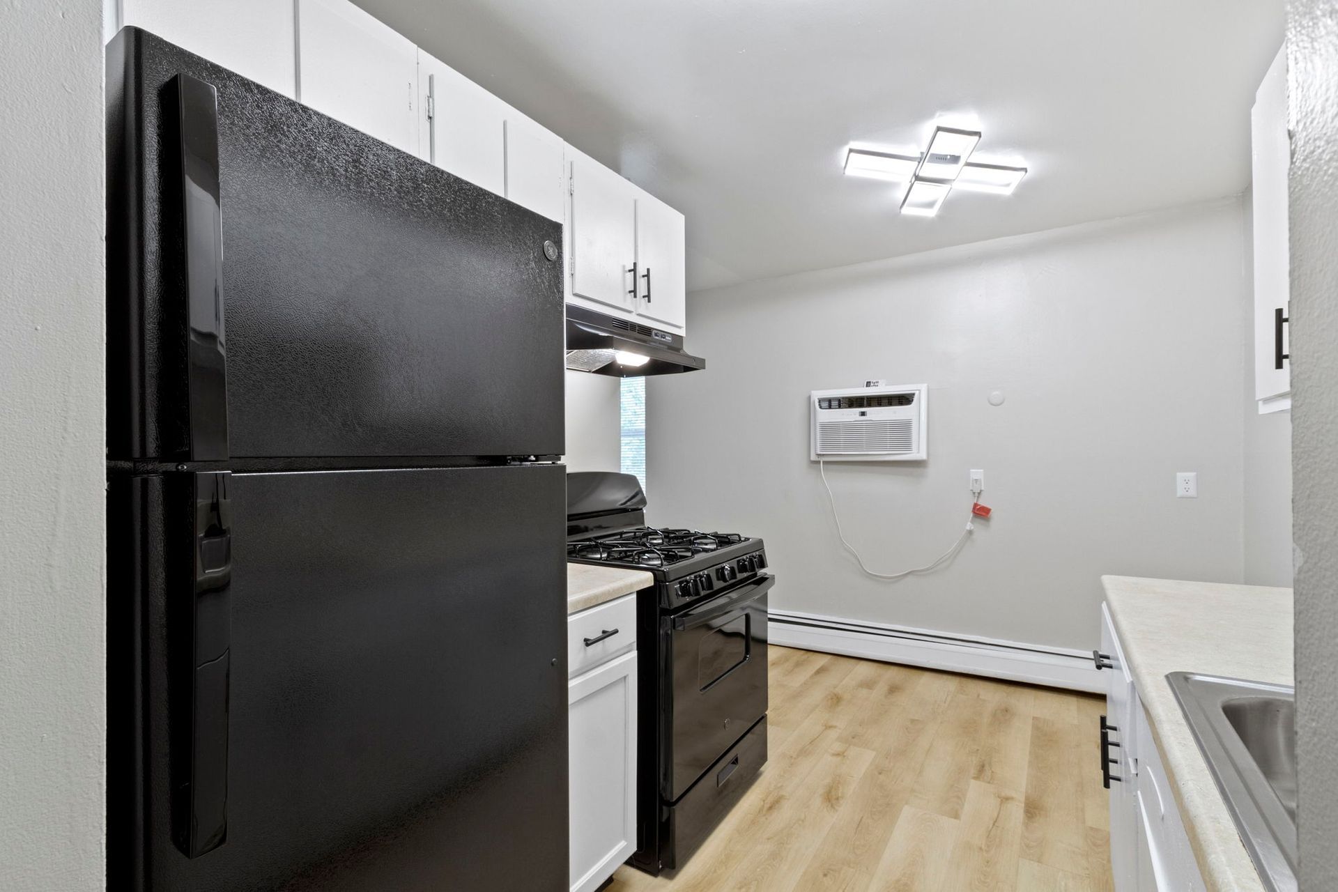 Black appliances in a small kitchen: refrigerator, stove, and cabinets with light wood-look flooring and white walls.