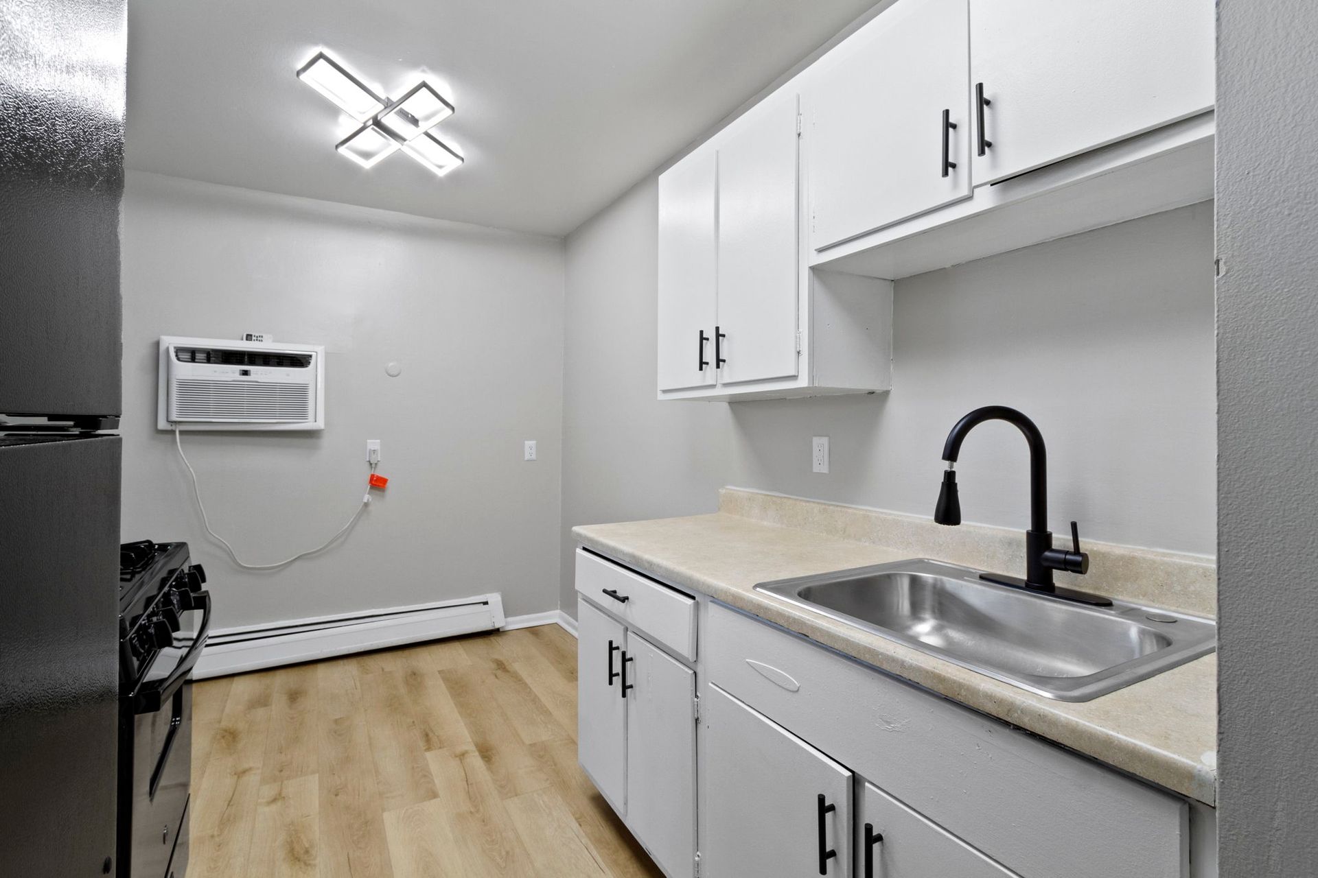 Small kitchen with white cabinets, black faucet, and wood-look flooring.