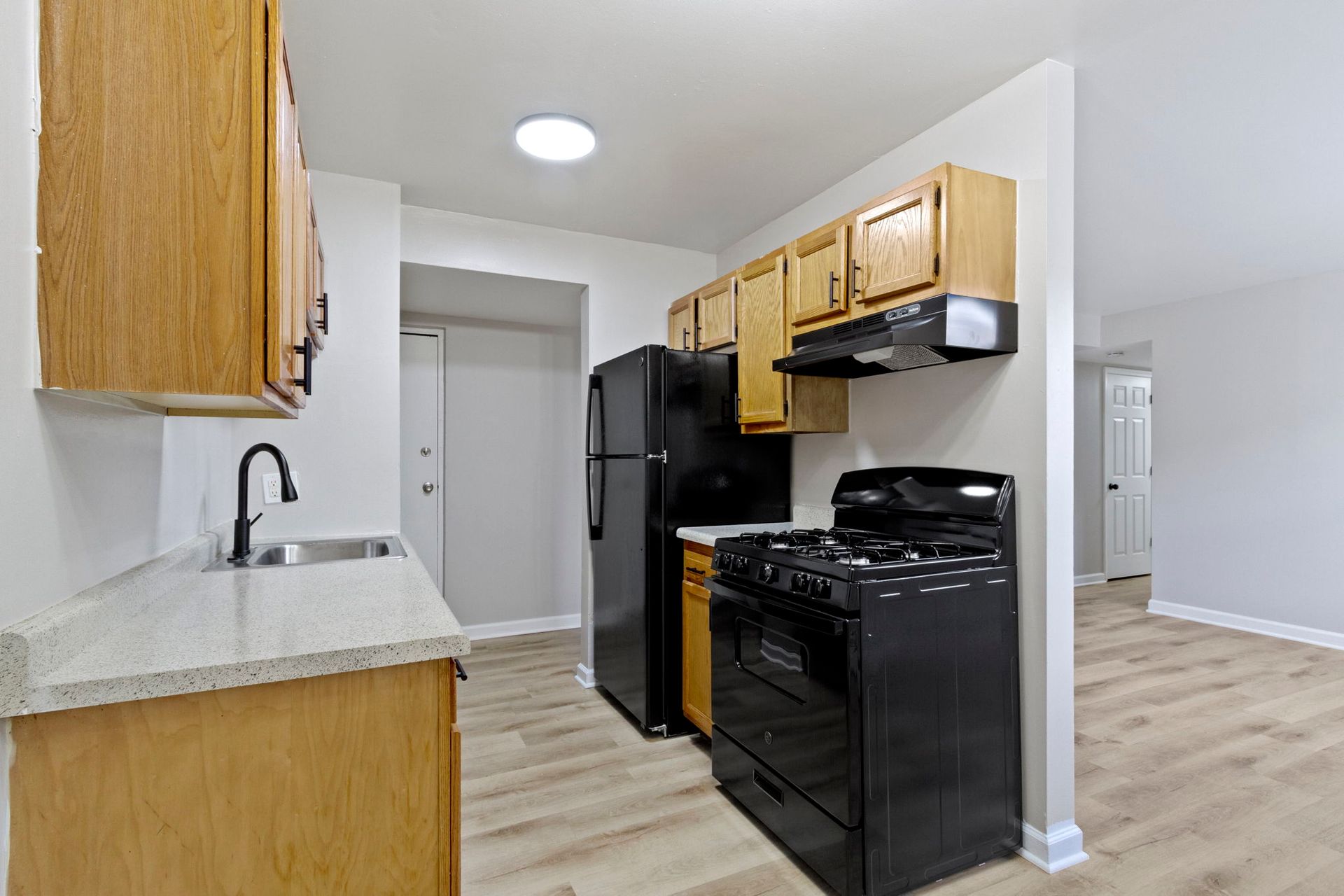 Kitchen with light wood cabinets, black appliances, and light wood floors.